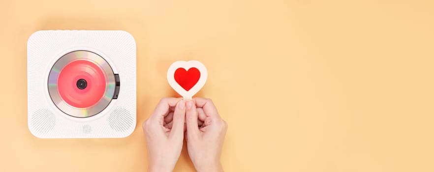 Hands holding heart shape red gift card next to white cd player with red disc on yellow background. Love music, Valentine day, Greeting, retro Love song, space for text