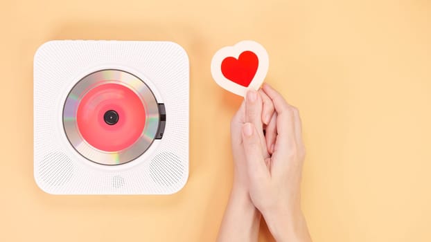 Hands holding heart shape gift card next to white cd player with red disc on yellow background. Love music, Valentine day, Greeting, retro Love song, space for text