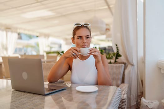 Woman coffee cafe laptop. Coffee break in cafe with sea view . Tranquil long haired woman drinking coffee in plant filled place. Woman sitting at a coffee shop with mobile phone drinking coffee