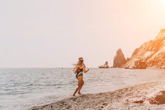 Woman travel summer sea. A happy tourist in a blue bikini enjoying the scenic view of the sea and volcanic mountains while taking pictures to capture the memories of her travel adventure