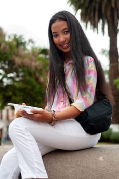 young girl from ecuador sitting on a monument in the city with a book in her hands and smiling at the camera. book day. High quality photo