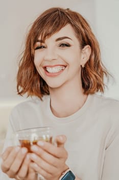 Woman drinks tea close-up. Portrait of a brunette in a white T-shirt with a transparent mug in her hands