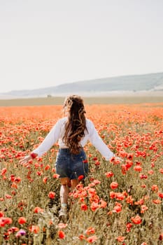 Woman poppies field. Back view of a happy woman with long hair in a poppy field and enjoying the beauty of nature in a warm summer day