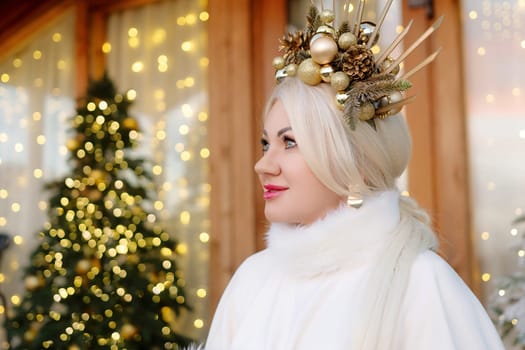 Happy blonde as Snow Maiden in white costume. Wooden house exterior Festive setting. Character with crown creating festive scene