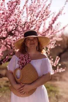 Woman blooming peach orchard. Against the backdrop of a picturesque peach orchard, a woman in a long white dress and hat enjoys a peaceful walk in the park, surrounded by the beauty of nature