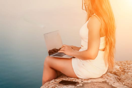 Freelance women sea working on the computer. Good looking middle aged woman typing on a laptop keyboard outdoors with a beautiful sea view. The concept of remote work