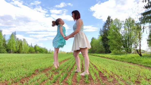 Happy mother and daughter enjoying rest, playing, fun and doing sports exercises on nature in a green field. Woman and girl resting outdoors in summer and spring day