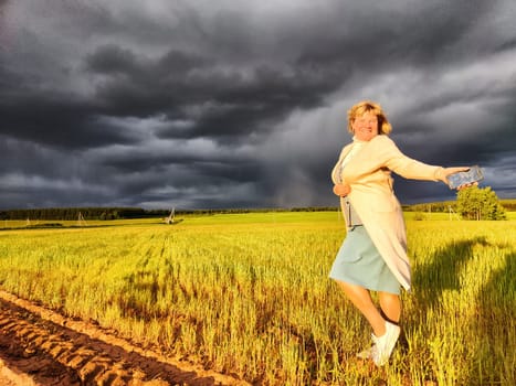 An adult girl in a field and with stormy sky with clouds posing for picture in the rain. A woman having fun outdoors on rural and rustic nature