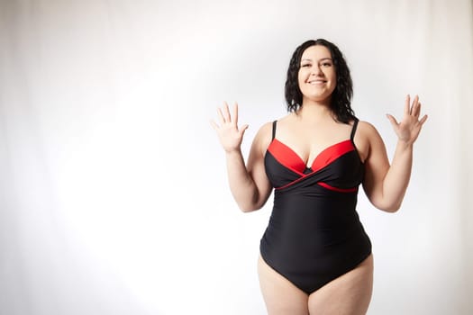 Portrait of attractive dreamy thick woman in red black swimsuit posing on white background. Body positive, photoshoot, selfie. Funny plus size model