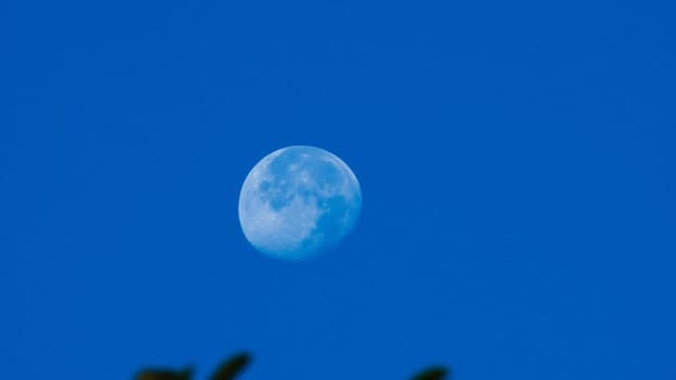 A beautiful moon was seen in the clear blue sky. Close-up of the moon in a light blue sky.