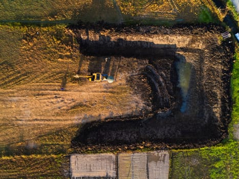 Excavating dirt into a dump truck to build a water storage pond for use in the dry season for agriculture. Aerial view of a backhoe is working.