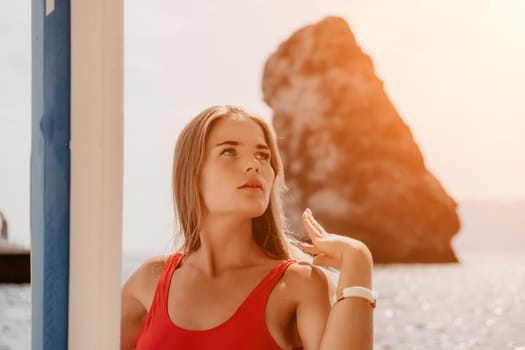 Close up shot of beautiful young caucasian woman with black hair and freckles looking at camera and smiling. Cute woman portrait in a pink bikini posing on a volcanic rock high above the sea