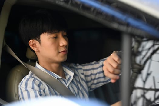 Young businessman checking time on wrist watch while driving to the office