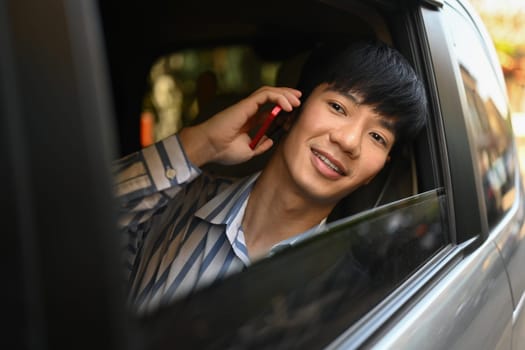 Cheerful young Asian man looking away while talking on mobile phone in car