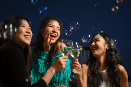 Group of cheerful female friends having fun toasting champagne and laughing together at the rooftop night outdoor party