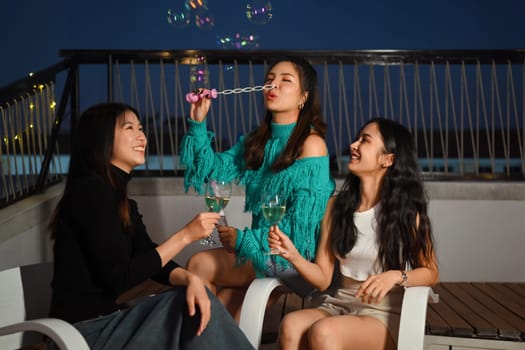 Young friends gathered together having fun toasting champagne and blowing soap bubbles at the rooftop night party