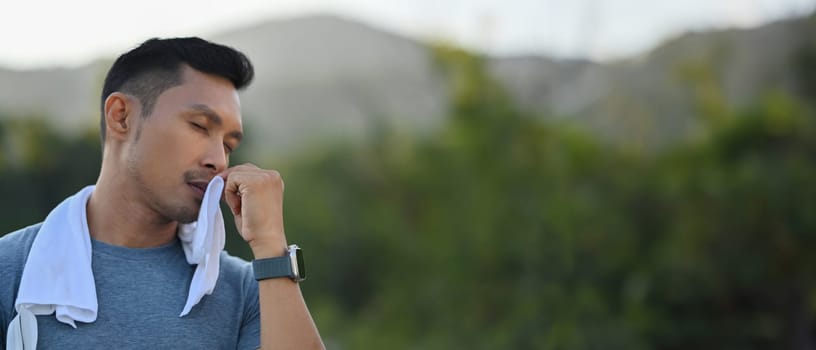 Young athletic man wiping sweat from his forehead during workout outdoors.