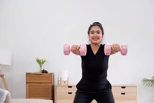 Fat woman exercising at home A beautiful oversized woman in a sports bra and casual pants stands in the living room and exercises..