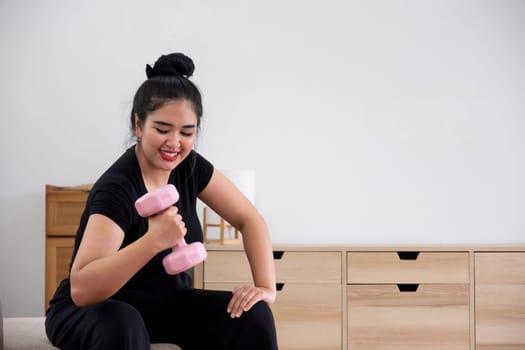 Fat woman exercising at home A beautiful oversized woman in a sports bra and casual pants sits in the living room and exercises