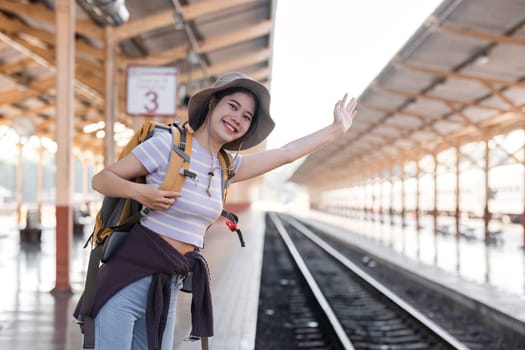 Cute Asian traveler woman carrying a suitcase waiting for the train at the train station.