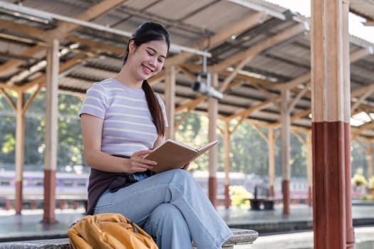 Young Asian woman in modern train station Female backpacker sitting on a bench reading a book while waiting for a train