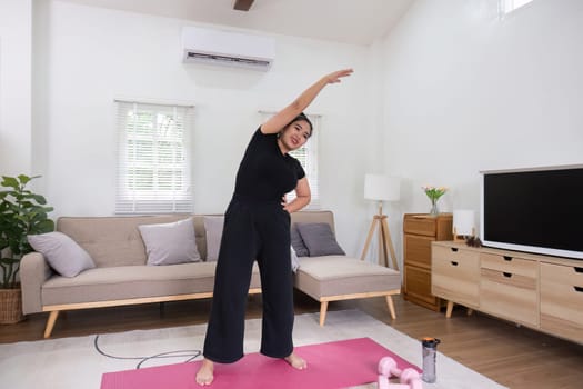 Fat woman exercising at home A beautiful oversized woman in a sports bra and casual pants stands in the living room and exercises..