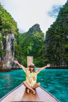 Happy Asian women in front of a longtail boat with hands up at Kho Phi Phi Thailand, women in front of a boat at Pileh Lagoon with turqouse colored ocean during a boat trip to Maya Bay Koh Phi Phi