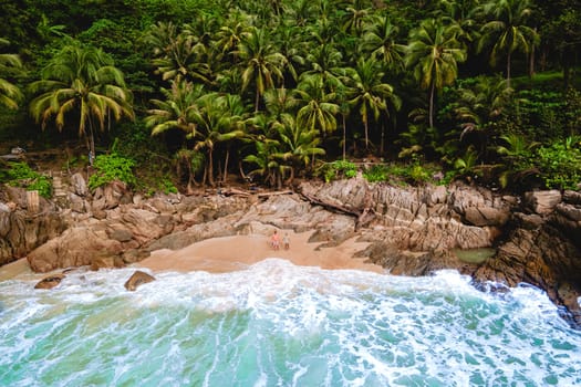 A couple of men and women are relaxing on a white tropical beach with palm trees in Phuket Thailand. Freedom Beach Phuket on a sunny day in Thailand