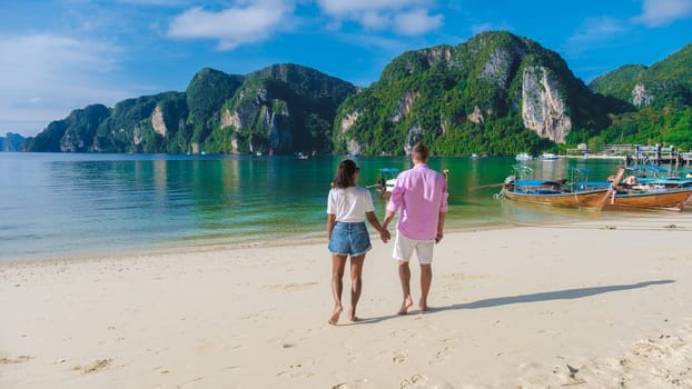 A couple of men and woman at Kho Phi Phi Thailand walking on the beach in the morning, sunny morning in Koh Phi Phi tropical Island in Thailand with longtail boats