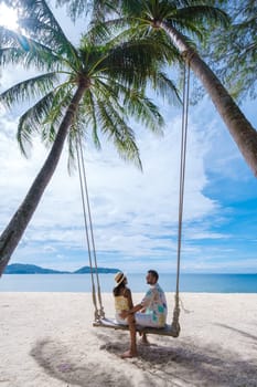 A couple of men and women are relaxing on a white tropical beach with palm trees in Phuket Thailand. men and woman in a rope swing under a palm tree