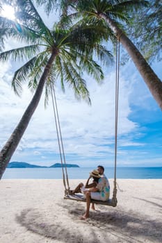 A couple of men and women are relaxing on a white tropical beach with palm trees in Phuket Thailand. men and woman in a rope swing under a palm tree
