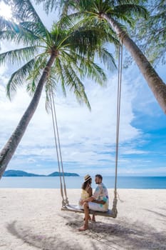 A couple of men and women are relaxing on a white tropical beach with palm trees in Phuket Thailand. men and women in a rope swing under a palm tree on a sunny day