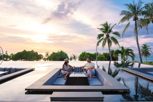 couple watching the sunset in an infinity pool on a luxury vacation in Thailand, man and woman watching the sunset on the edge of a pool in Thailand on vacation