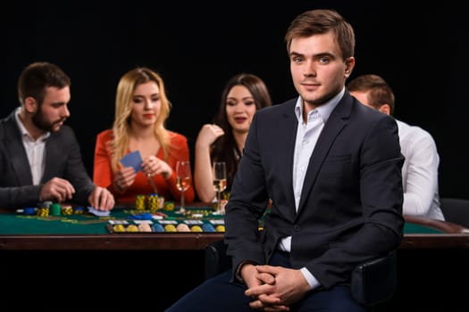 Young people playing poker at the table. Handsome man sitting in the foreground. Casino