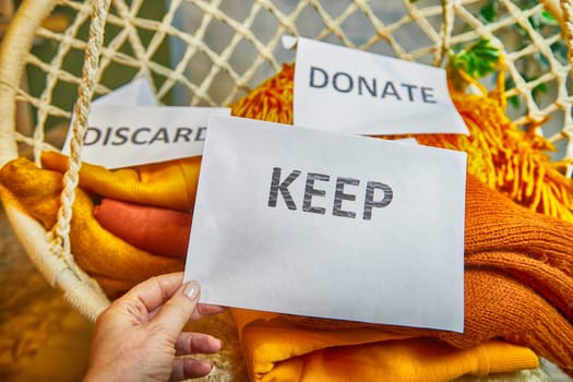 Signs with the words keep, donate, discard and fashion clothes folded in stacks in cozy room. The concept of cluttering and decluttering. Background