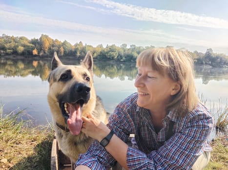 Adult girl with shepherd dog taking selfie in forest. Middle aged woman and big shepherd dog on nature. Friendship, love, fun, hugs