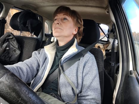 Portrait of female driver in solo journey. Adult mature woman holding steering wheel and looking through windscreen in travel by vehicle on vacation. Lady girl who is owner or rent car for travel