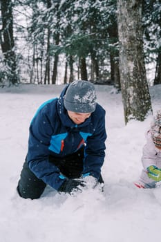 Dad and little child make a snowman while squatting in a snowy forest. Cropped. High quality photo