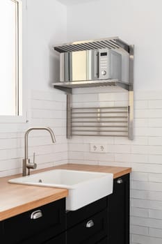 View of a white modern kitchen sink with dark countertops and cabinets and rails and white tiles on window background. The concept of a modern kitchen in a new building.
