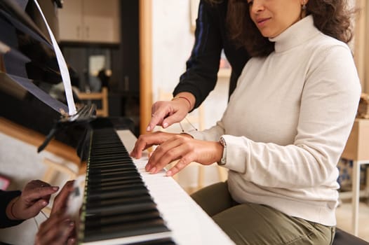 Close-up portrait of pretty young adult Latin American woman learning playing grand piano with her teacher, a talented pianist musician during music class. People. Arts. Culture. Lifestyle. Education