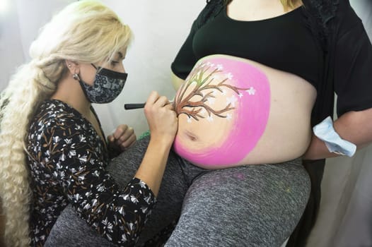 Body painting session on the belly of an eight month pregnant woman. Drawing of a tree