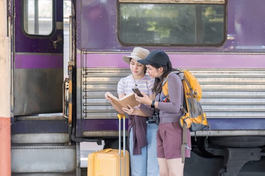 Two Asian female tourist friends are at the train station. Waiting for the train to travel to the provinces together on the weekend..