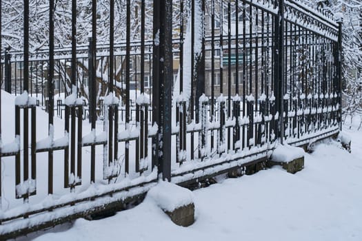 Photo a metal fence is a high black fence. Forged gate fence. In winter, in snow and snowdrifts.