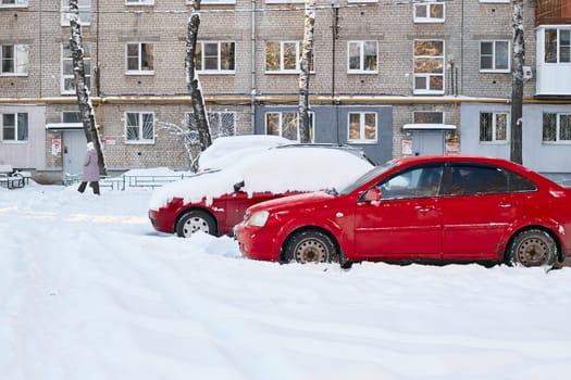 Photo two red cars on the background of a multi-storey brick house and a man. Urban winter landscape.
