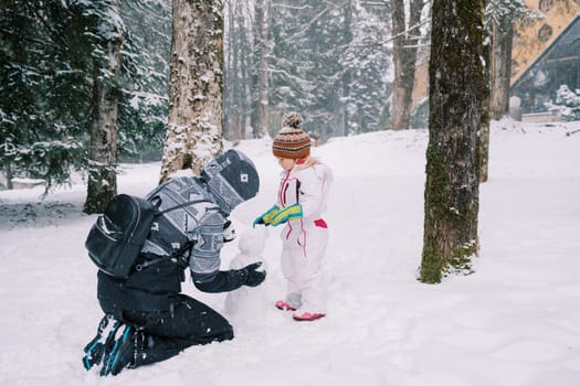 Little girl helps her mother sculpt a snowman in a snowy forest. High quality photo