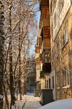 Photo balconies and windows of a brick five-storey building next to trees in winter. Snow and snowdrifts.