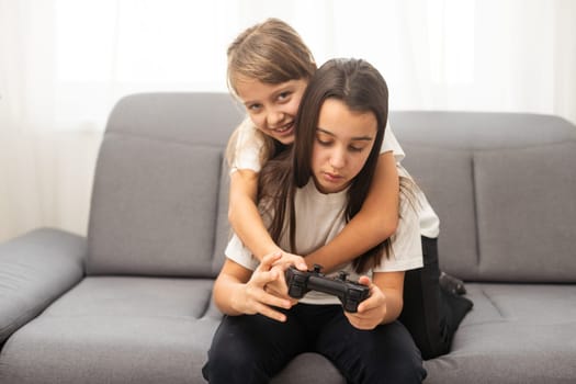 Two little girlfriends playing video game with joysticks. Excited and focused european children. Childhood concept. Entertainment and leisure. Idea of friendship. Grey background in studio. Copy space. High quality photo