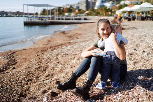 Little girl hugging her mother with a lunchbox in her hand on a pebble beach. High quality photo