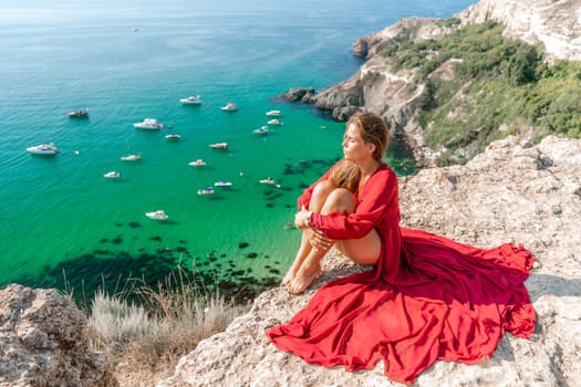 Woman red dress sea. Happy woman in a red dress and white bikini sitting on a rocky outcrop, gazing out at the sea with boats and yachts in the background