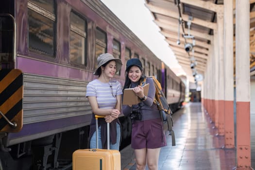 Two Asian female tourist friends are at the train station. Waiting for the train to travel to the provinces together on the weekend..